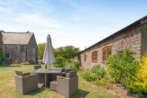 A stone building with a garden patio featuring wicker furniture and an umbrella.