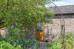 A stone building with a wooden door and a garden with various plants.