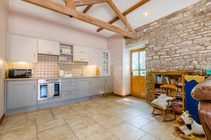 A kitchen with a stone wall, wooden beams, and a bookshelf with books.