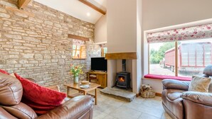 A cozy living room with stone walls, a fireplace, leather sofas, and a television. - 2 Bed in Awre (oc-o45277) (Awre)
