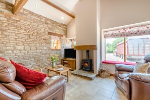 A cozy living room with stone walls, a fireplace, leather sofas, and a television. - 2 Bed in Awre (oc-o45277) (Awre)