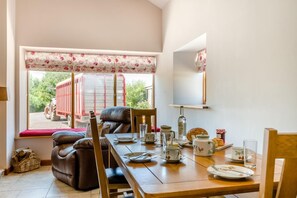 A dining area with a table set for two, a window with a view of a red vehicle outside, and a mirror on the wall.