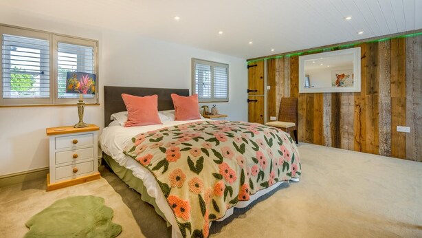 A bedroom with a bed, bedside tables, a lamp, a chair, and a wooden wall panel. - 5 Bed in Marhamchurch (oc-p45735) (Marhamchurch)