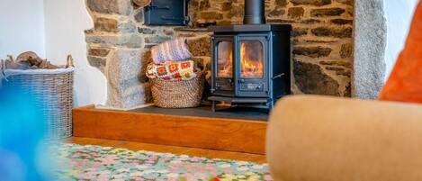 A cozy room with a stone wall, a wood-burning stove, a wicker basket, and a floral-patterned rug.