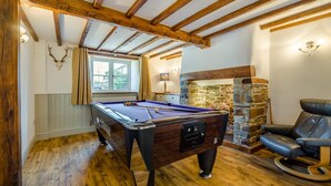 A pool table in a room with wooden beams, a stone fireplace, and a leather chair. - 5 Bed in Marhamchurch (oc-p45735) (Marhamchurch)