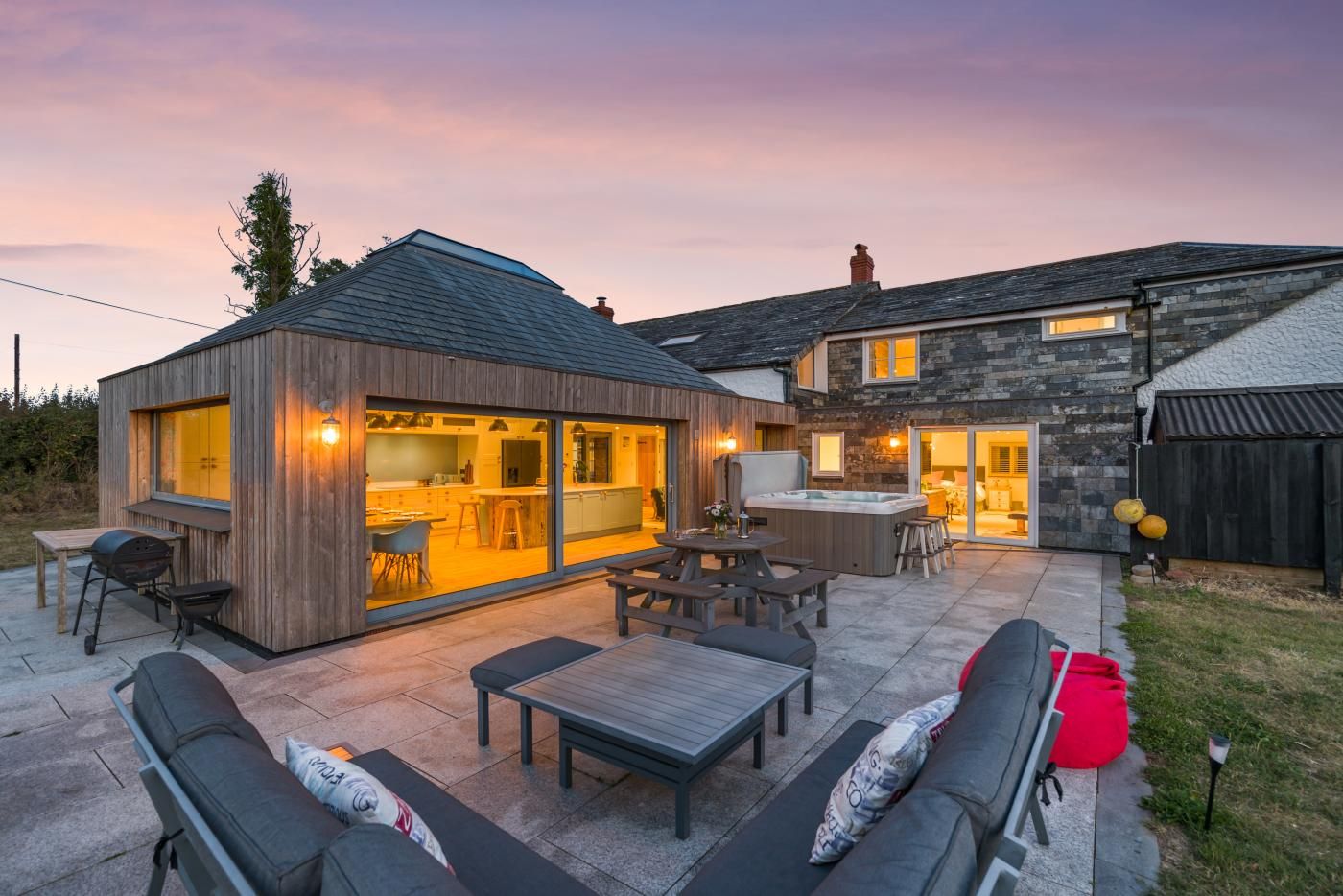 A modern house with a patio area featuring outdoor furniture, a hot tub, and a kitchen with large windows.