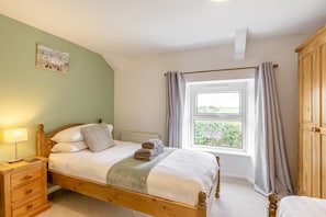 A bedroom with a wooden bed, a bedside table with a lamp, a window with curtains, and a view of greenery outside. - 3 Bed in Maxworthy (oc-s45407) (Maxworthy)