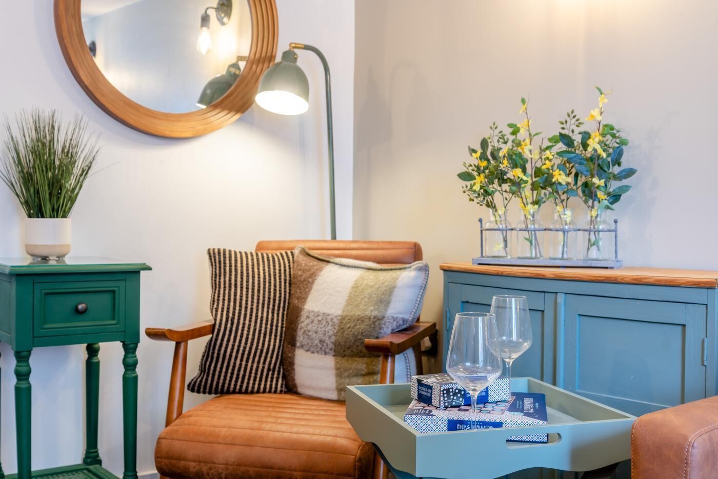 Un rincón acogedor con una silla, una mesita con un vaso y un jarrón decorativo con flores.