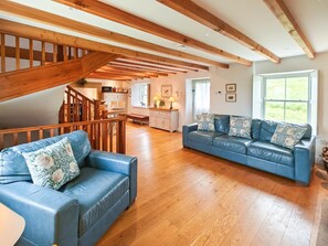 A spacious living room with a wooden staircase, a blue leather sofa set, and a dining area. - 3 Bed in Slaggyford (oc-h44976) (Slaggyford)