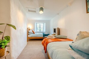 Ein schmaler Flur, der in ein Schlafzimmer mit Bett, Nachttisch und Fenster führt.