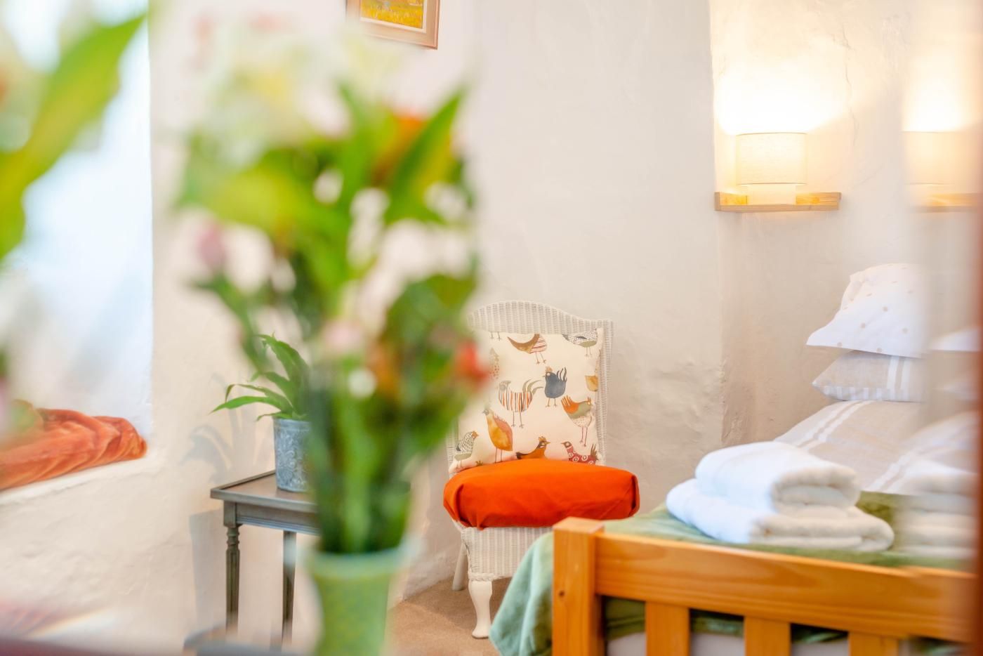 A room with a bed, a chair, a small table, and a wall-mounted lamp.
