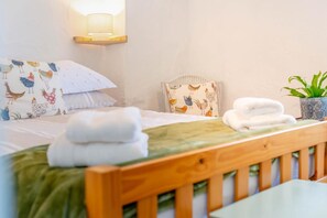 Ein ordentlich gemachtes Bett mit gefalteten Handtüchern, einer Wandlampe und einem Blumentopf.