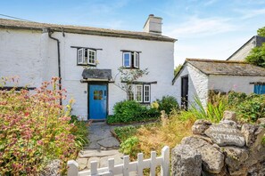 Ein weißes Cottage mit blauer Tür, einem Kiesweg und einem weißen Zaun.