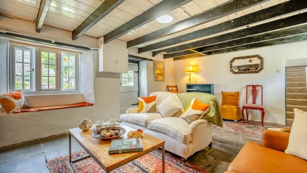 Uma sala de estar acolhedora com um sofá, poltronas, uma mesa de centro e um tapete. Há uma janela com vista para o verde lá fora.