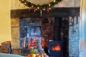 Une cheminée en pierre avec un feu allumé, entourée de fruits et d’une guirlande de Noël.