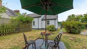 A patio with two chairs and a table under a green umbrella, a wooden fence, and a white building in the background. - 1 Bed in St. Dogmaels (oc-m45322) (Saint Dogmaels)