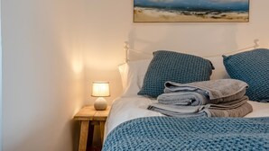 A bed with a blue blanket, pillows, and a folded towel. There is a painting of a beach scene on the wall above the bed. - 1 Bed in St. Dogmaels (oc-m45322) (Saint Dogmaels)