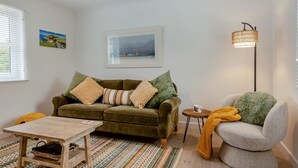 A living room with a green sofa, a grey armchair, a small wooden table, and a floor lamp. - 1 Bed in St. Dogmaels (oc-m45322) (Saint Dogmaels)