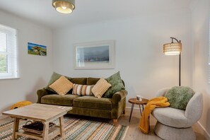 A living room with a green sofa, a grey armchair, a small wooden table, and a floor lamp. - 1 Bed in St. Dogmaels (oc-m45322) (Saint Dogmaels)