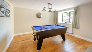 Een pooltafel in een kamer met houten vloeren, een klok aan de muur en een raam met gordijnen.