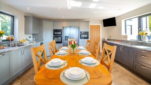 Een moderne keuken met een eettafel voor zes personen, voorzien van roestvrijstalen apparatuur, een flatscreen televisie en een groot raam dat natuurlijk licht binnenlaat.