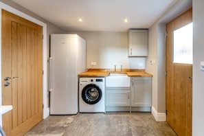 A compact kitchen with a washing machine, a sink, and wooden cabinets. - 4 Bed in Llansannan (oc-p44897) (Llansannan)