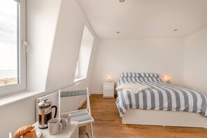 A bedroom with a bed, bedside tables, a window, and a kitchenette area with a coffee maker and mugs.