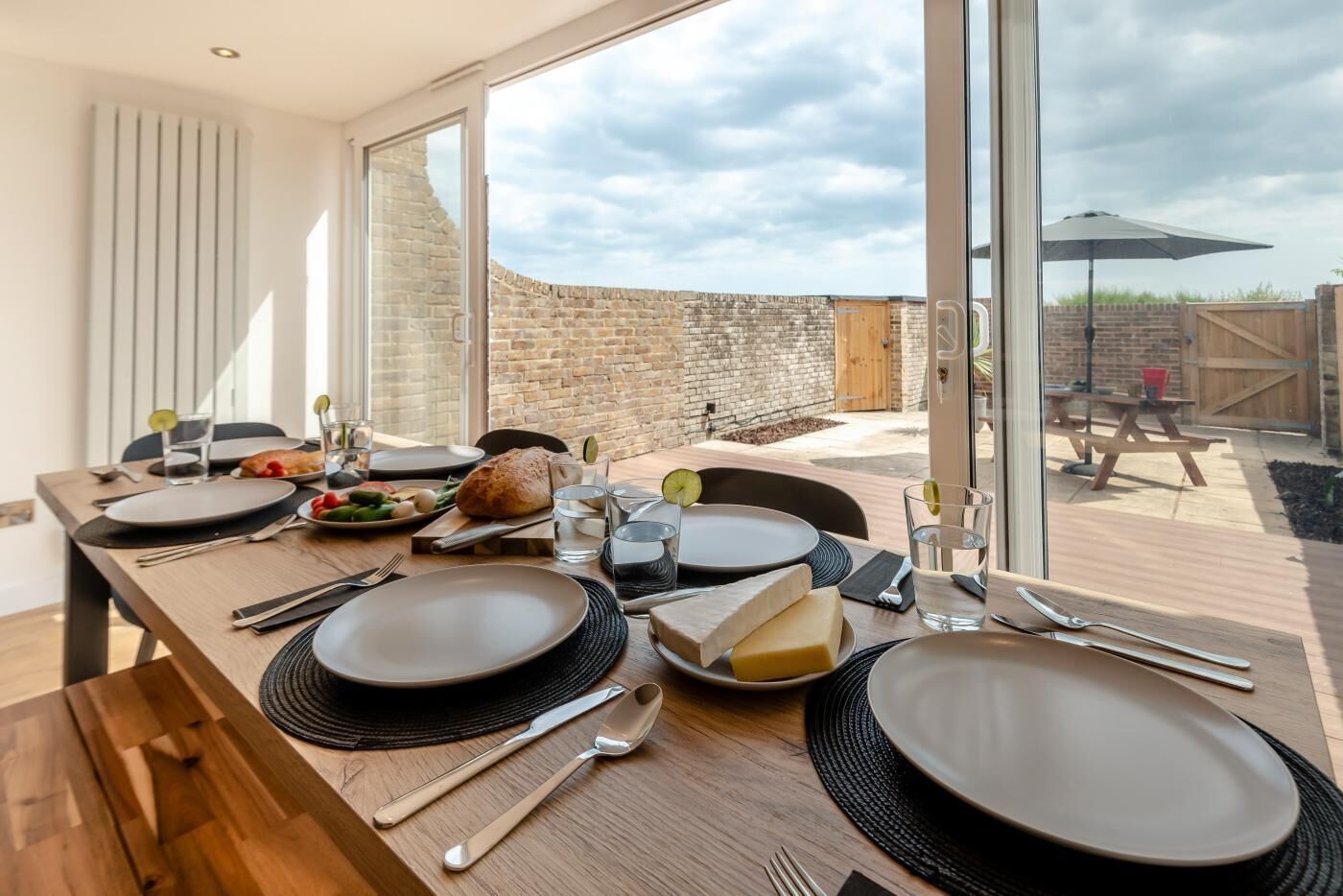 A dining table set with plates, cutlery, and food, overlooking a stone wall and outdoor seating area.
