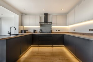 A modern kitchen with dark cabinetry, a central island, and under-cabinet lighting. - 3 Bed in Rustington (oc-p45430) (Rustington)