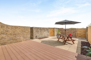 A patio area with a wooden deck, a picnic table, and an umbrella.