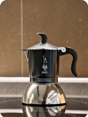Een roestvrijstalen FIAMMETTA INDUCTION espressomachine met een zwarte hendel en een logo op het deksel.