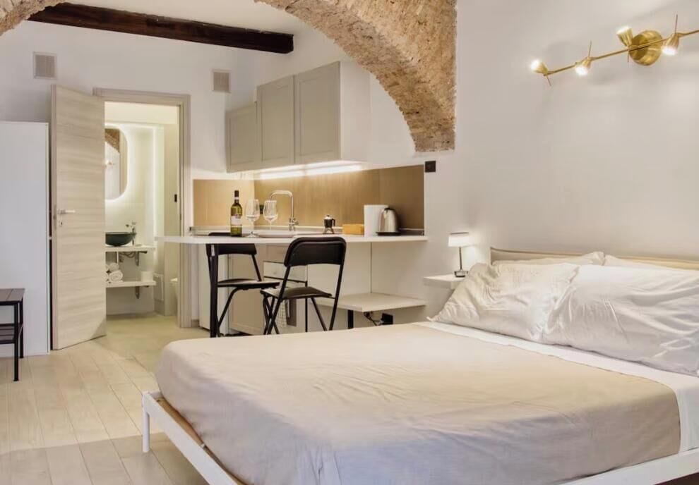 Ein Schlafzimmer mit einem Bett, einem Schreibtisch und einem Stuhl. Es gibt eine Küchenzeile mit einem Spülbecken und einer Arbeitsplatte.