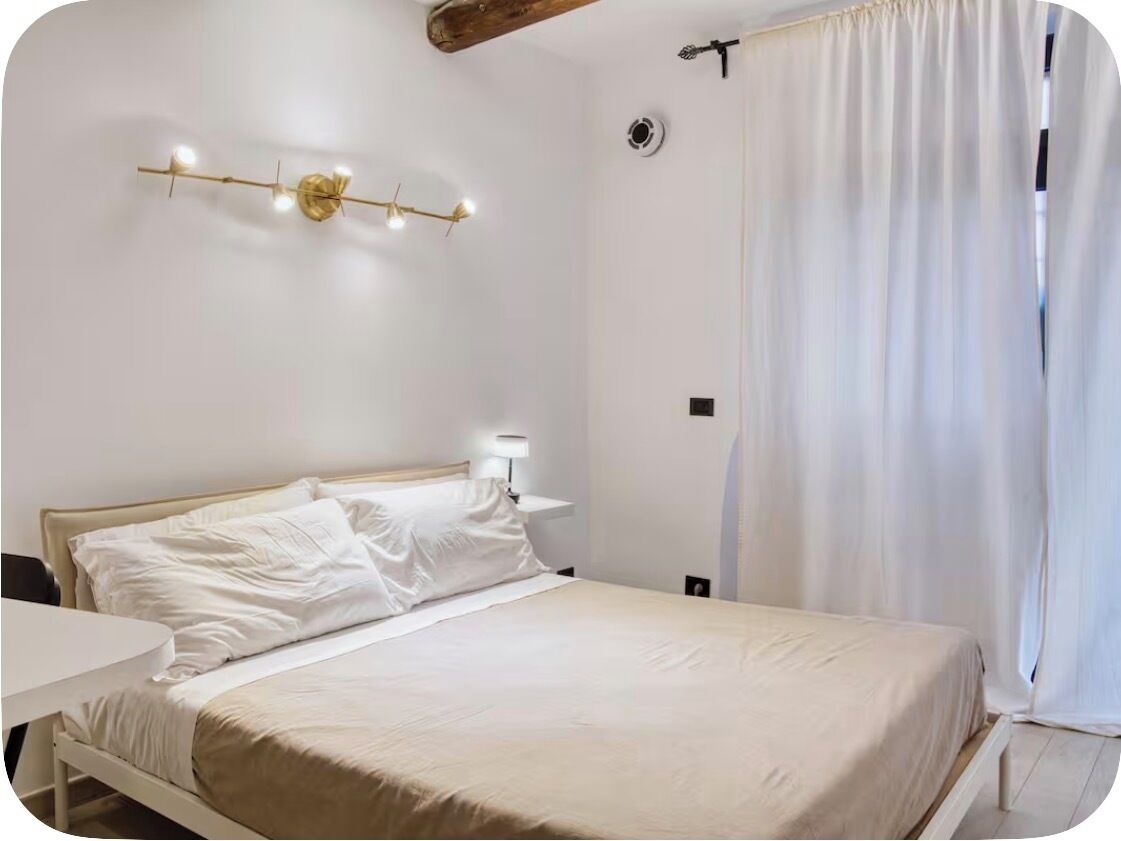 A bedroom with a bed, bedside table, lamp, and a wall-mounted light fixture.