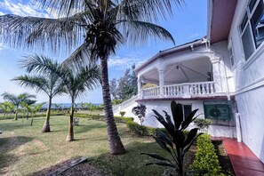 A white building with a balcony, surrounded by palm trees and a well-maintained lawn. - Kisuri White House - Luxury Beach Home in Mfangano with A/C (Homa Bay County)