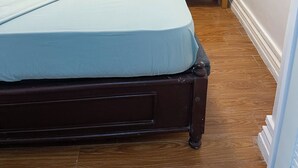A bedroom with a bed, a wooden nightstand, a window with curtains, and a wall-mounted air conditioning unit.