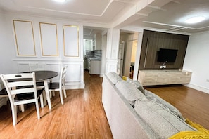 A modern living room with a sofa, a dining table with chairs, and a kitchen in the background.