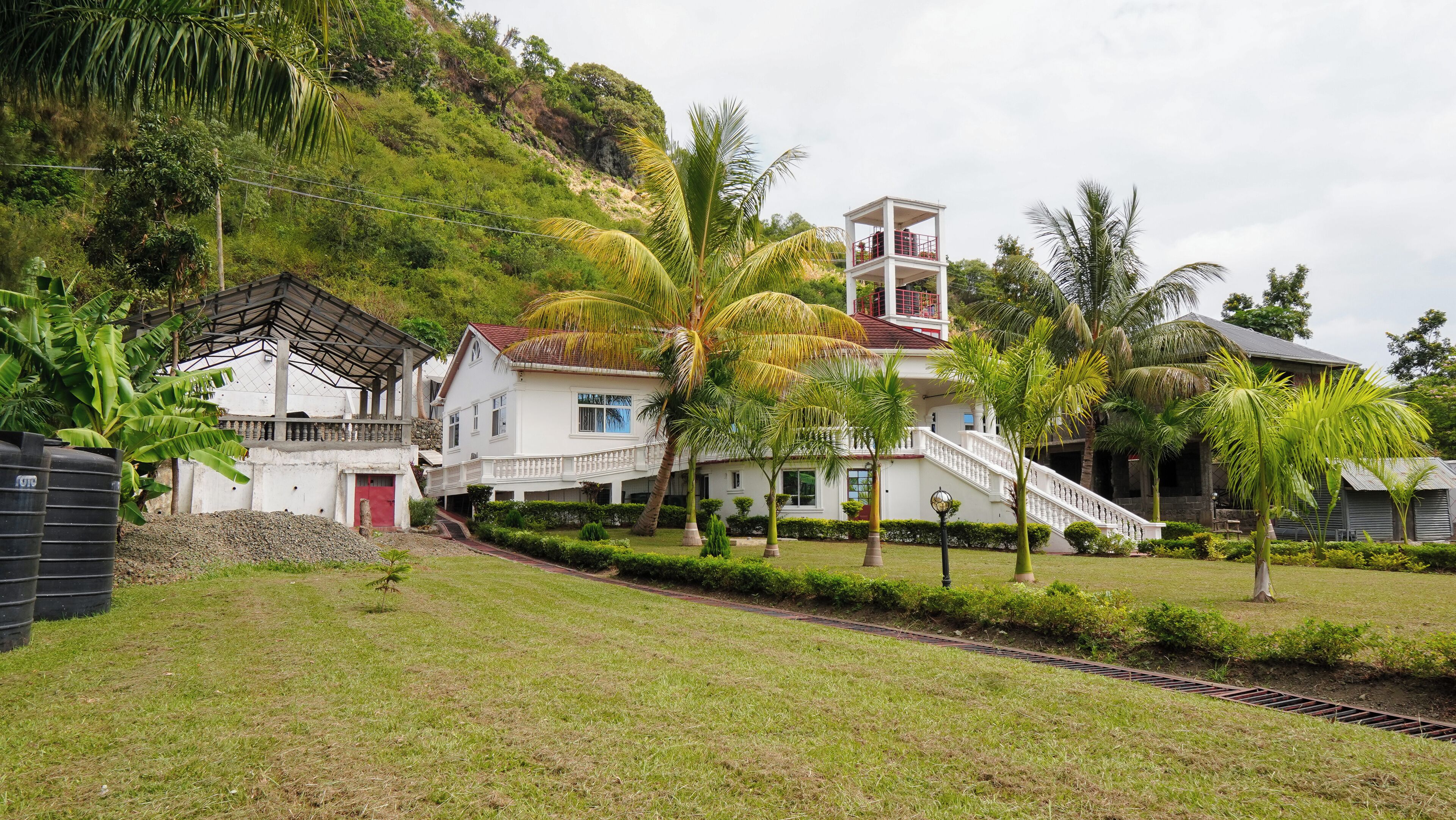 A two-story building with a red door, surrounded by lush greenery and palm trees.