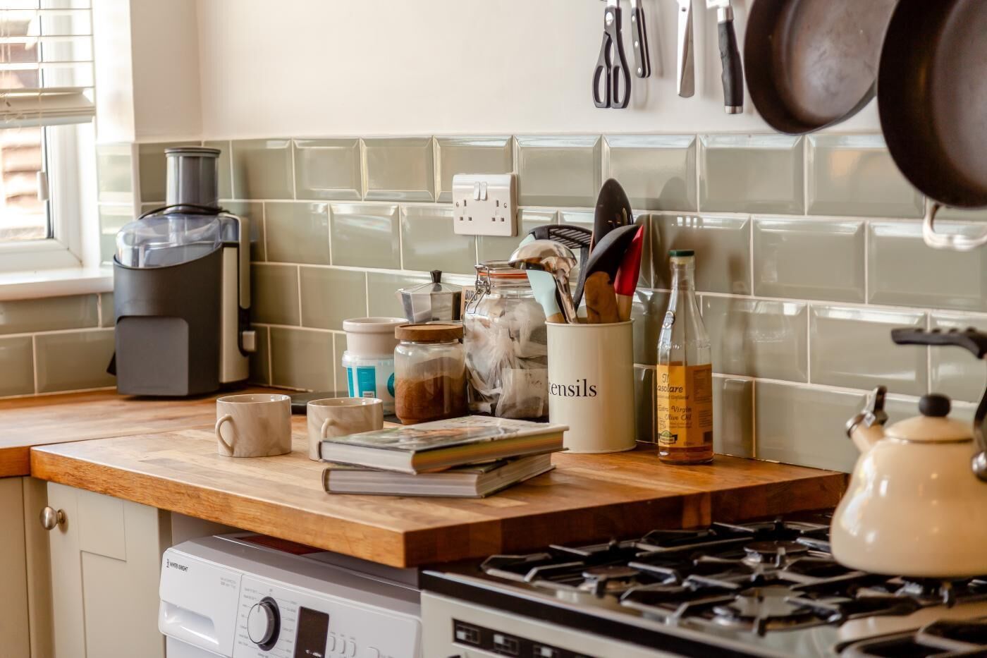 A kitchen with a coffee maker, jars, utensils, and a kettle on the counter.