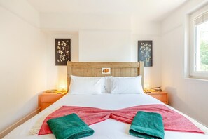 Ein Hotelzimmer mit hölzernem Kopfteil, weißer Bettwäsche, zwei Nachttischen und Bildern an den Wänden.