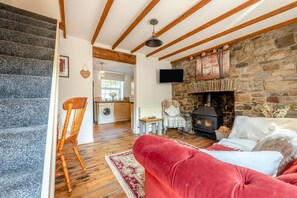A cozy living room with a stone fireplace, a red sofa, and a wooden staircase.