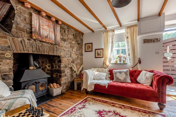 A cozy room with a stone fireplace, a red sofa, a chessboard, and a window with curtains. - 2 Bed in Upper Cwmtwrch (oc-s45449) (Cwm-twrch Uchaf)