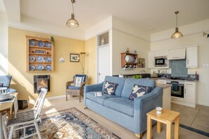 Ein Wohnzimmer mit blauem Sofa, einem Esstisch und einer Küchenzeile mit modernen Geräten.