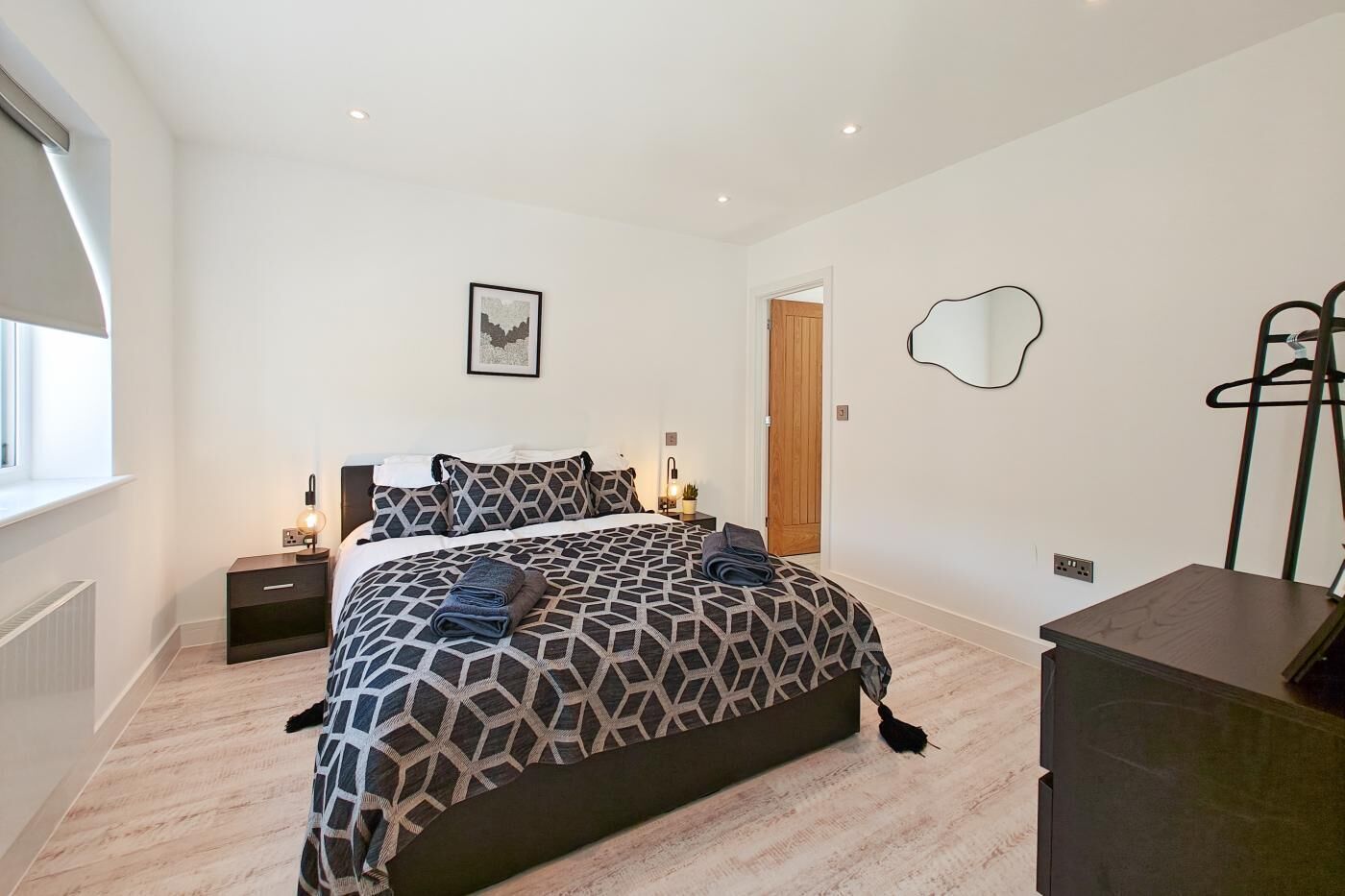 Een slaapkamer met een bed, nachtkastjes, een spiegel, een radiator en een raam.
