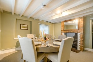 A dining room with a brick fireplace, a round table set for six, and a window with patterned curtains. - 3 Bed in Snettisham (oc-d45398) (Snettisham)