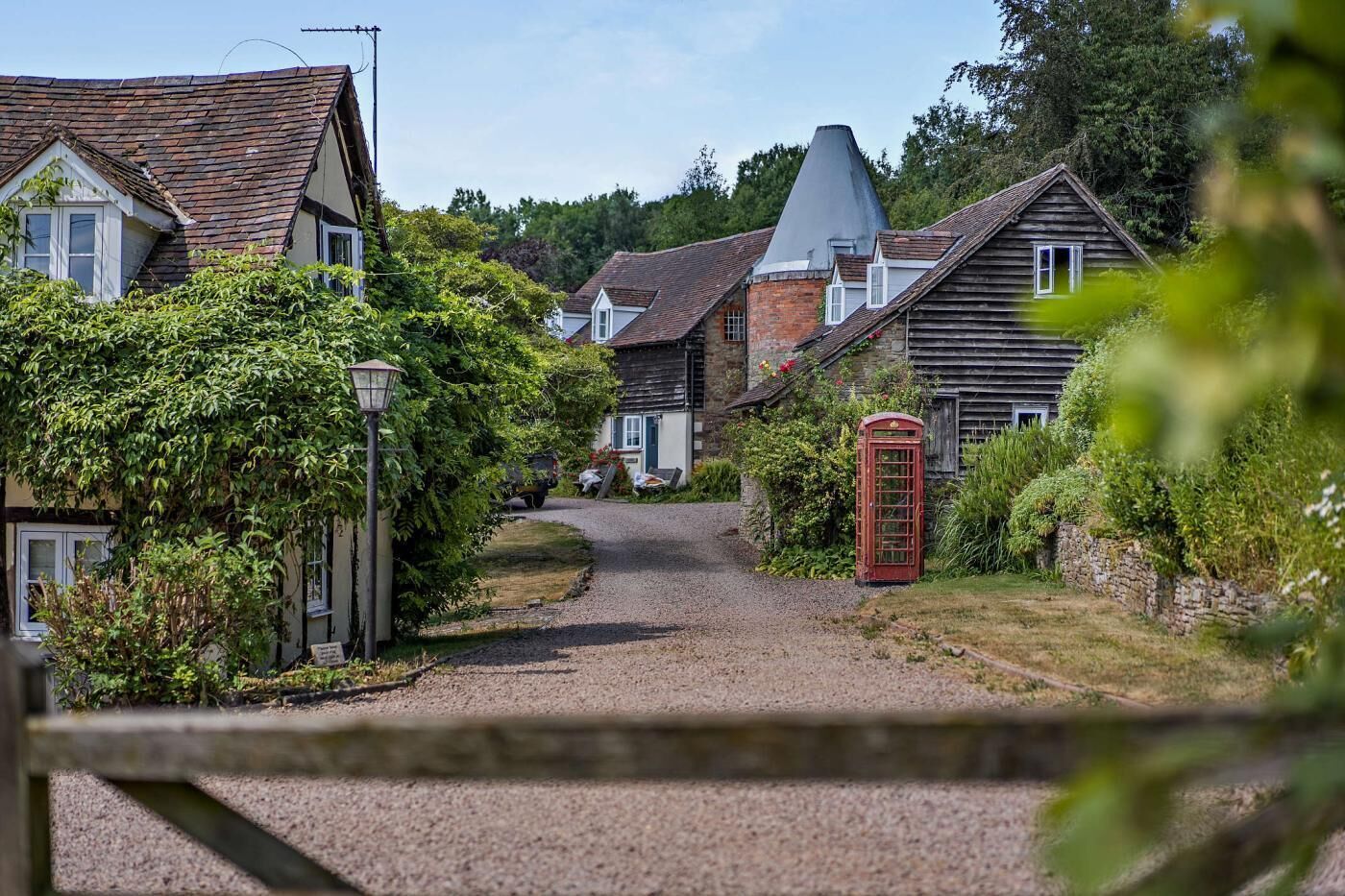 A rural village street with traditional houses, a gravel path, and a red telephone booth.