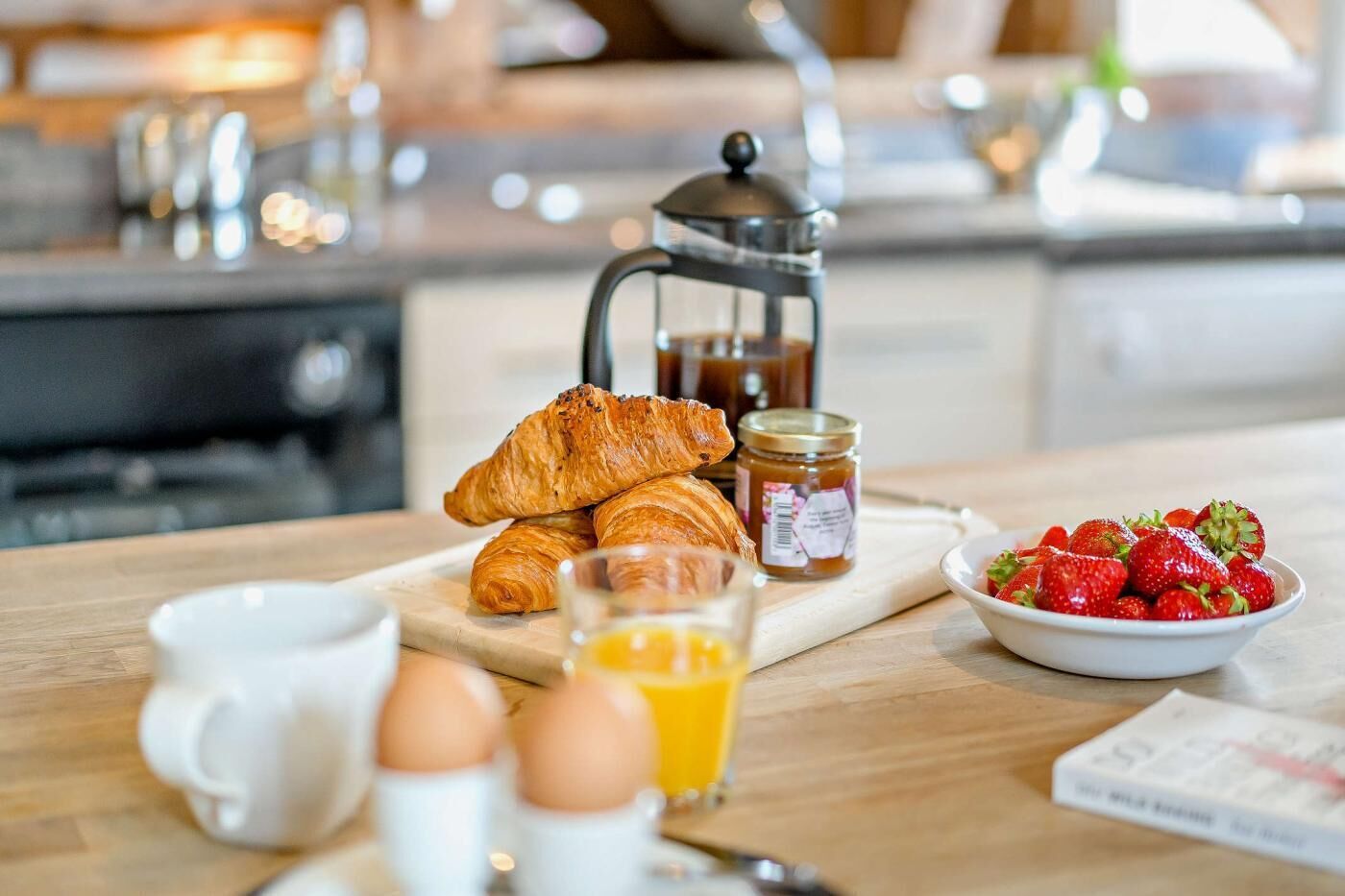Mesa de madeira com disposição para o café da manhã: croissants, morangos, jarra de café e um copo de suco de laranja.