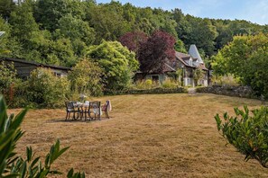 A grassy backyard with a dining table and chairs, surrounded by trees and a house. - 2 Bed in Cradley (oc-s45721) (Cradley and Storridge)