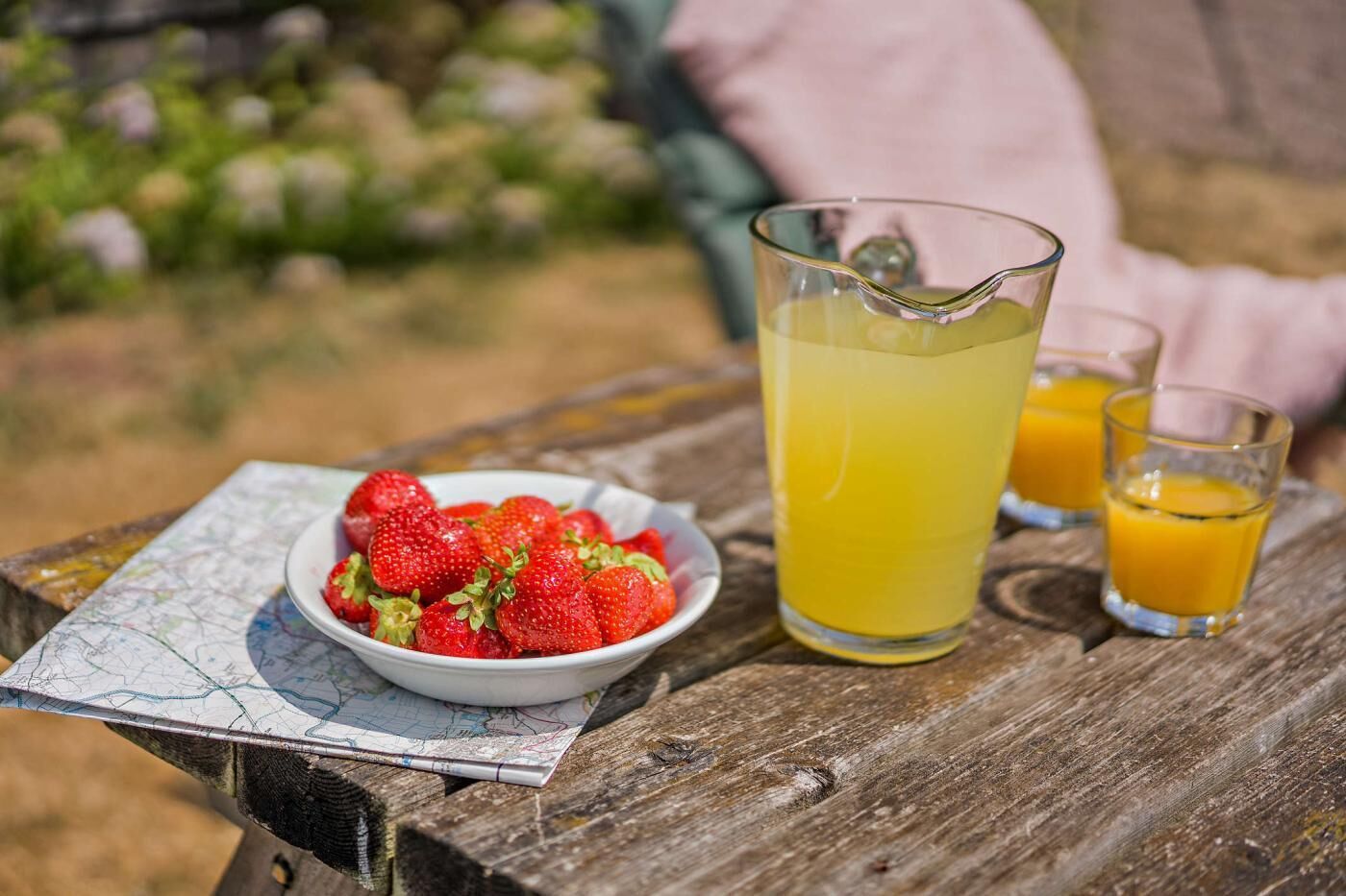 Ein Holztisch mit einer Schale Erdbeeren, einer Karaffe Orangensaft und zwei Gläser Orangensaft.