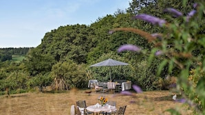 An outdoor dining area with a table and chairs, surrounded by lush greenery and a hill in the background. - 1 Bed in Cradley (oc-s45723) (Cradley and Storridge)