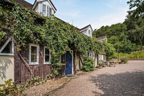 A rustic building with a wooden exterior, a blue door, and a gravel driveway. - 1 Bed in Cradley (oc-s45723) (Cradley and Storridge)